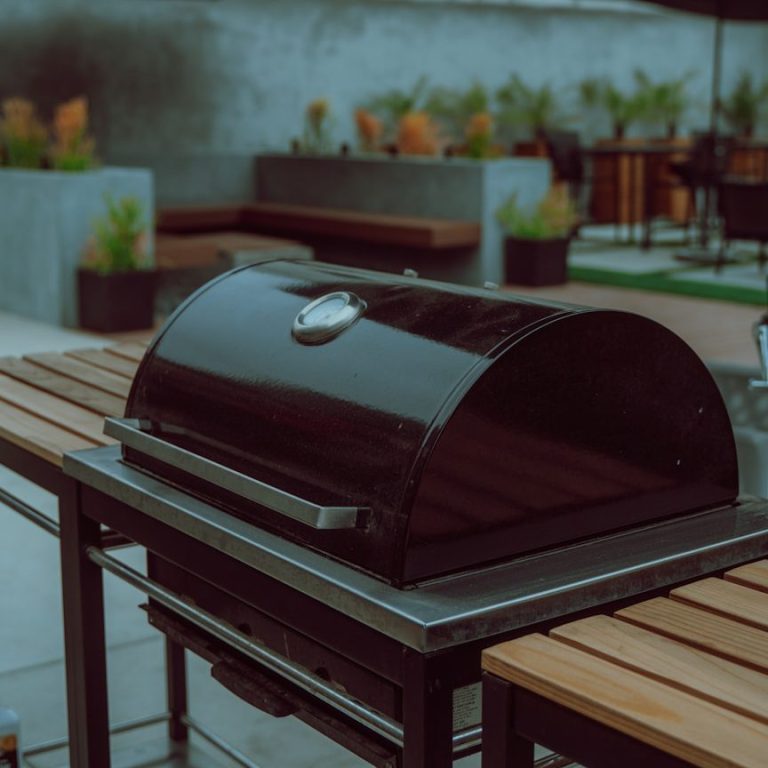 Einbaugrill Schwarzer Grill auf einem Tisch aus Holz, umgeben von Pflanzen und Sitzbereichen.