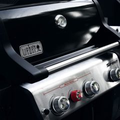 Ein moderner Grill mit silbernem Metall und schwarzen Bedienelementen.