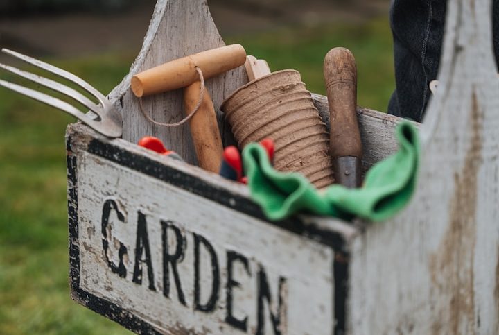Gartenwerkzeuge in einer Holzkiste, darunter eine Gabel, Schaufel und Schnur.
