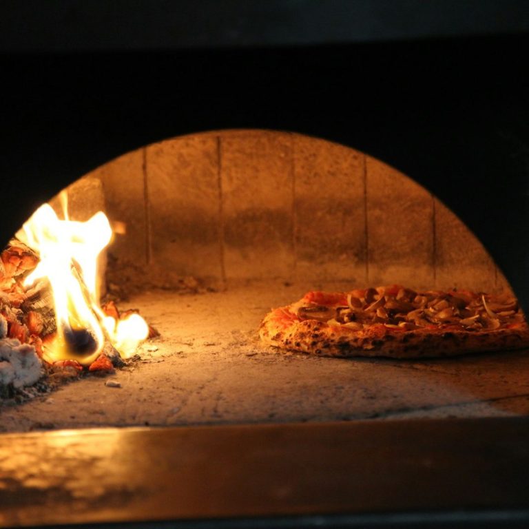Pizzaofen Pizza wird in einem Holzofen mit leuchtenden Flammen gebacken.