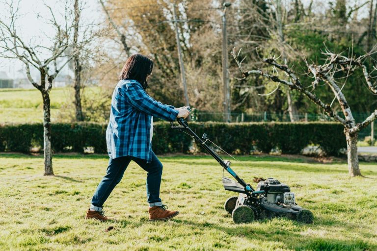 Eine Person vertikutiert den Rasen in einem Garten mit einem Vertikutierer.