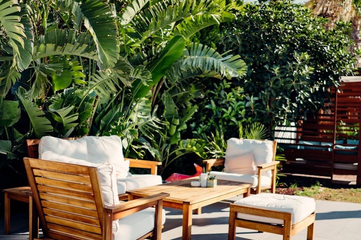 Holzmöbel mit bequemen Kissen, umgeben von üppigem Grün in einem Garten.