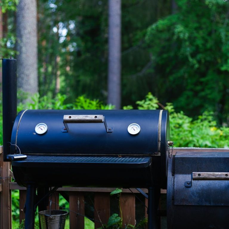 Pelletgrill Schwarzer Grill im Garten, umgeben von Bäumen und grünem Laub.