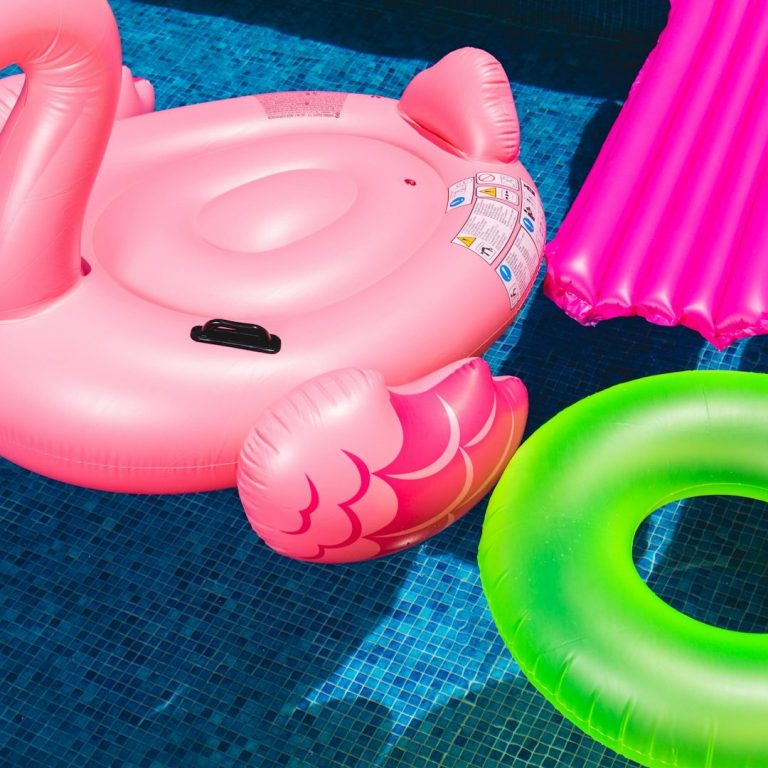 Poolzubehör Bunte Wasserlilien: rosa Flamingo, grüner Schwimmreifen und pinke Luftmatratze.