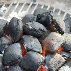 Glimmende Holzkohle auf einem Grill, mit glühenden Stellen und grauem Ascheüberzug.