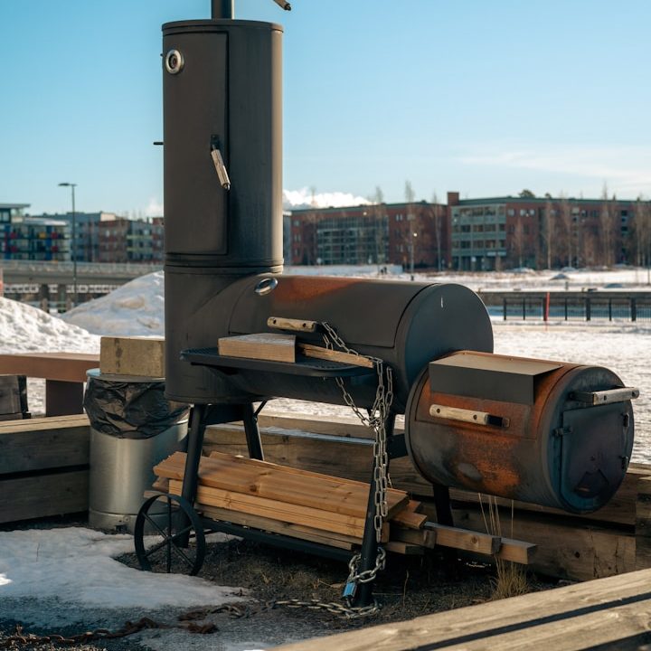 BBQ Smoker Schwarz-grauer Grill auf einer Holzterrasse mit Mülltonne im Hintergrund.