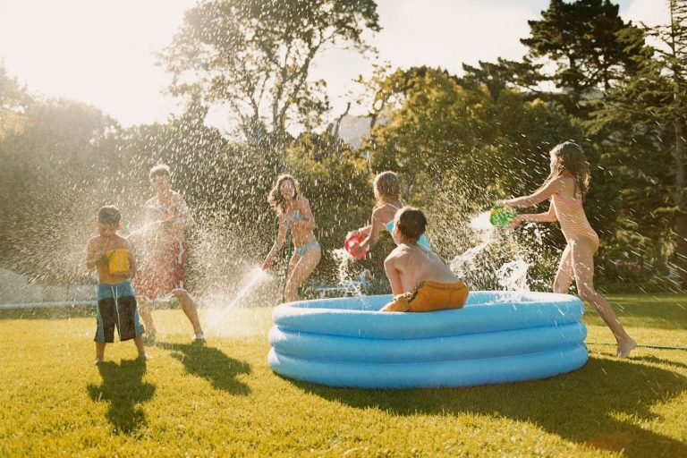 Kinder spielen im Garten mit Wasser in einem aufblasbaren Pool.